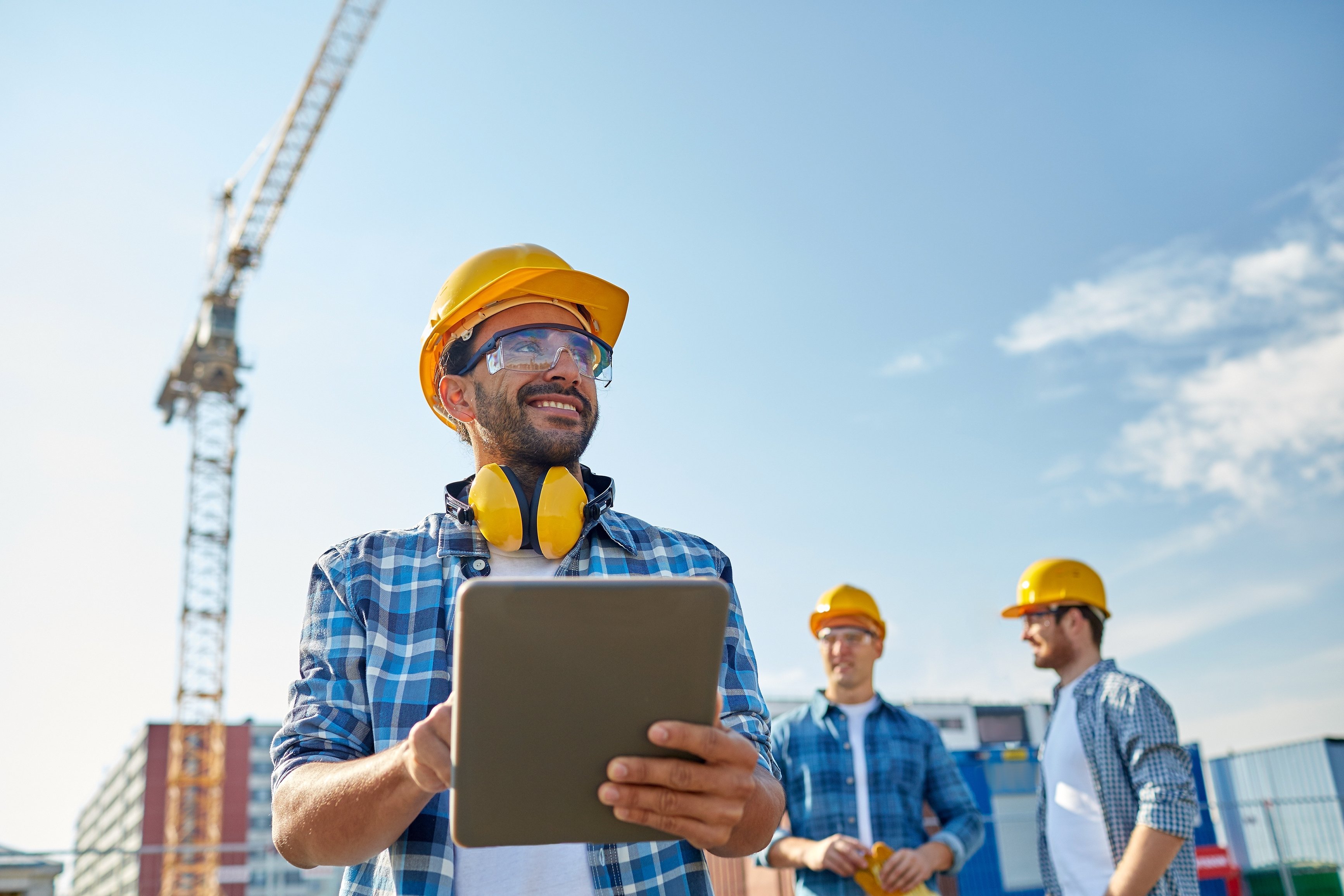 Construction worker smiles while holding iPad on construction site